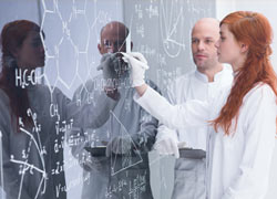 Two scientists drawing chemical formulae at a whiteboard