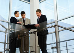 Group of people in suits standing together at the top of a staircase looking at a report 